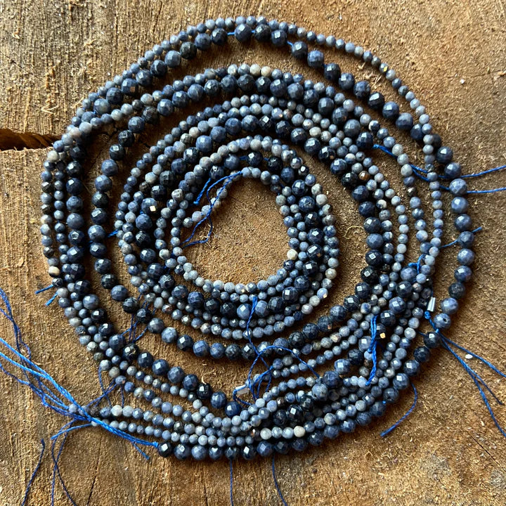 un sirag de margele de safir de culoare albastru inchis pe un suport rotund de lemn