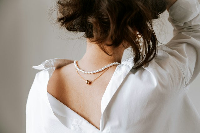 Layered pearl and delicate necklaces styled with an open white shirt